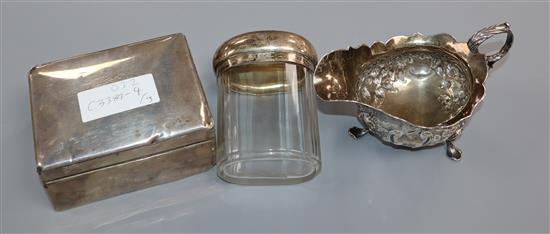 A George III silver sauce boat, a silver cigarette box and silver mounted glass toilet bottle.